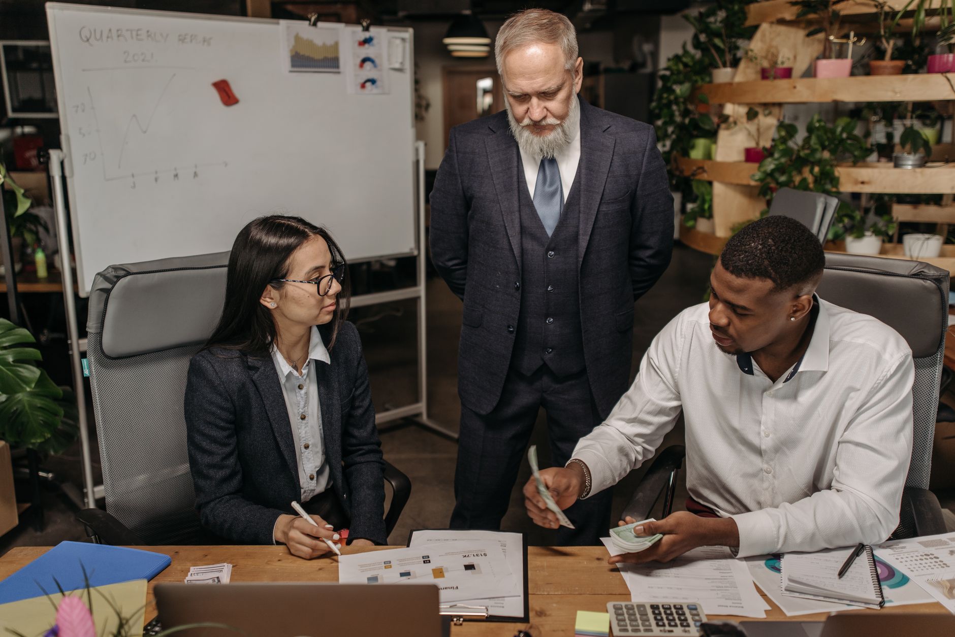 Three business professionals discussing reports at an office desk.